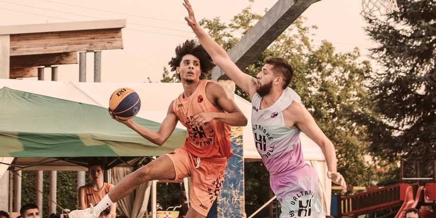 Due uomini che giocano a basket durante il Valtrighe Basketball Tournament nel Windows Court, palleggiando e tirando a canestro con intensa concentrazione e determinazione.